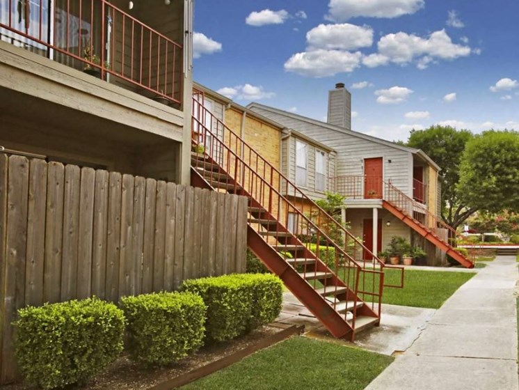 apartment exterior with green shrubs, grey and red staircases leading to red front doors